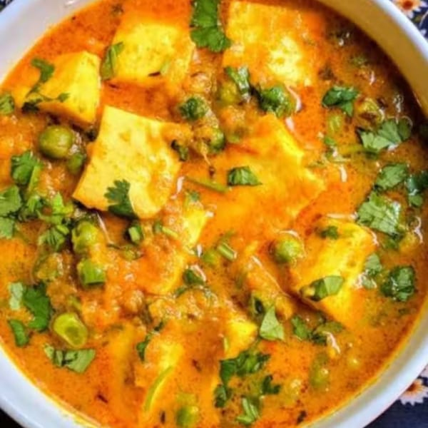 Close-up of a vibrant orange Indian curry with paneer, green peas, and fresh cilantro.