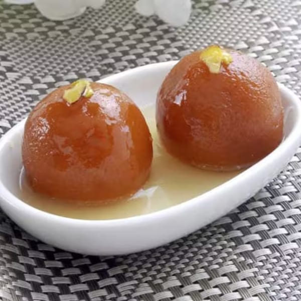 Two gulab jamun, Indian fried dough balls in syrup, garnished with pistachios in a white dish.