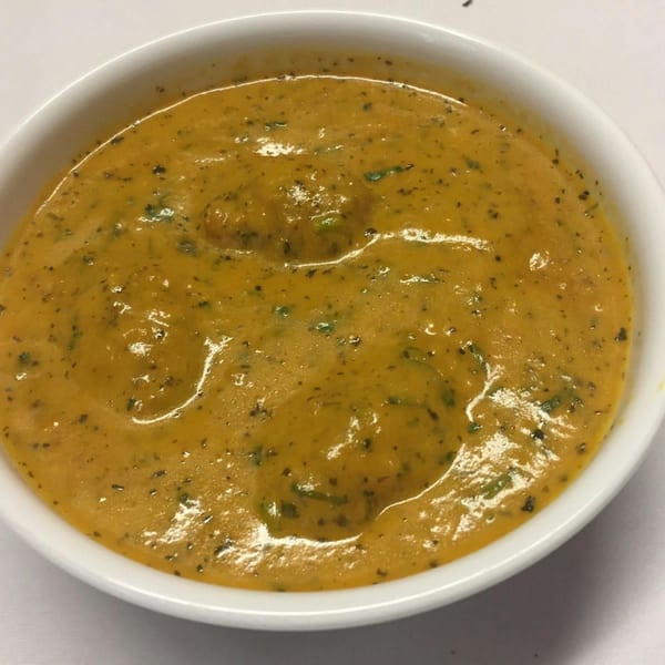 A white bowl filled with a rich, orange Indian curry, garnished with green herbs.