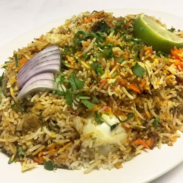 A plate of Indian biryani with rice, vegetables, cilantro, red onion, and a lime wedge.
