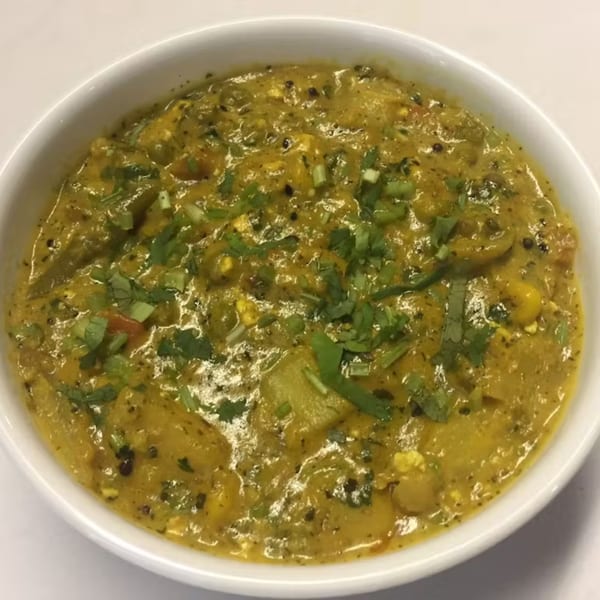 Close-up of a vibrant yellow Indian curry, garnished with fresh green herbs in a white bowl.