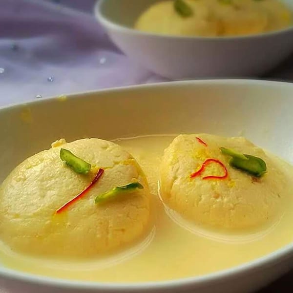 Two bowls of Rasmalai, an Indian dessert, garnished with saffron and pistachios.
