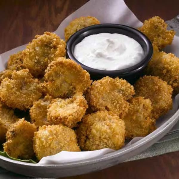 Golden-brown breaded mushrooms with a side of creamy white dipping sauce on a gray plate.